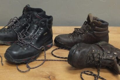 Two pairs of Zamberlan Boots, one black and one brown, sit on a wooden surface with their laces untied. Showing signs of decades of testing and use, these hiking boots tell a story of countless adventures.