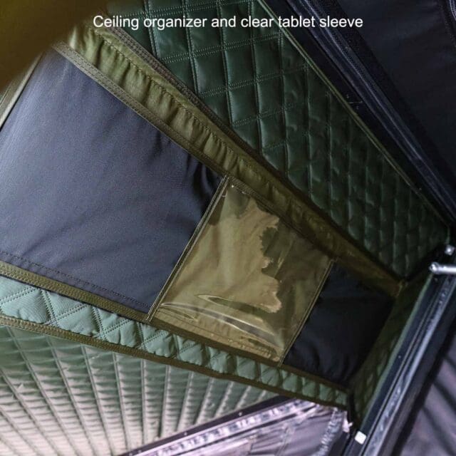 Close-up view of a quilted green ceiling organizer with a transparent tablet sleeve, attached to a tent roof. White text at the top reads, Ceiling organizer and clear tablet sleeve—perfect for your next Overland News adventure.
