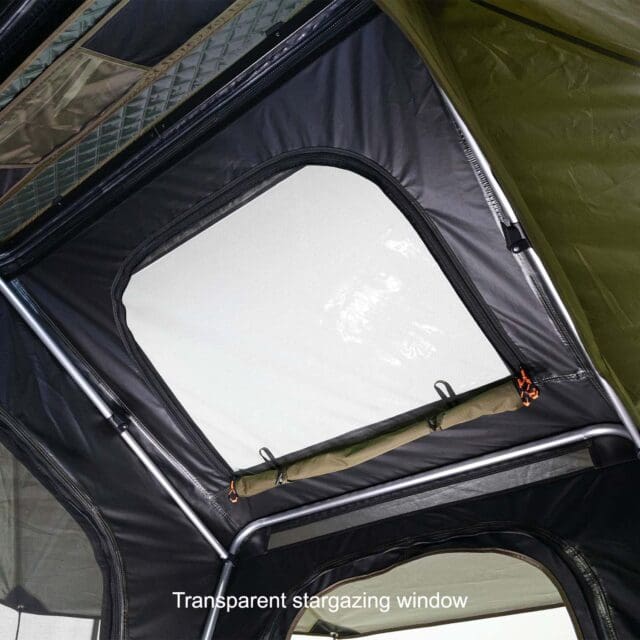 View from inside a tent looking up at a transparent rectangular window in the ceiling, framed by black and green fabric with metal poles. Text at the bottom reads, Transparent stargazing window—featured in Overland News.