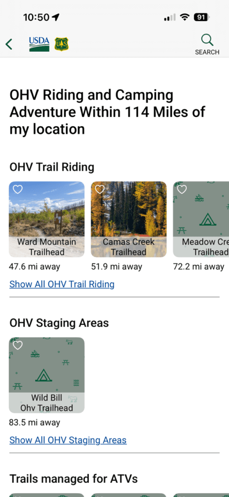 A mobile app screen displays Forest Service OHV riding and camping locations near the user, listing trailhead and staging area options with distances: Ward Mountain (47.6 mi), Camas Creek (51.9 mi), Meadow Creek, and Wild Bill (83.5 mi).