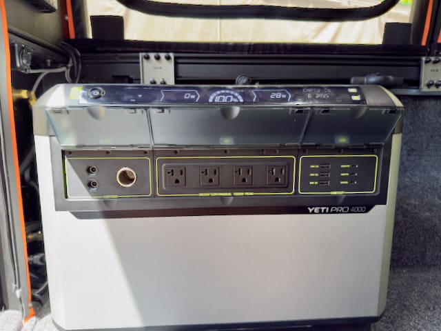 A Yeti Pro 4000 portable power station is shown inside a 2024 Toyota Tundra with an Alu-Cab Alu-Cabin. Its front panel features four AC outlets, various ports, a digital display, and indicator lights in the enclosed storage space.