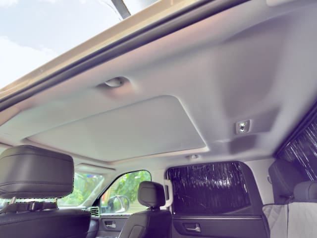 The photo shows the interior roof of a Toyota Tundra, featuring a closed sunroof, black seats, and a partially visible window with sunlight coming through.