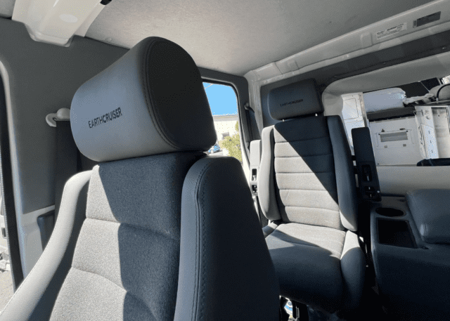 Two gray, cushioned van seats with EarthCruiser branding are shown inside a bright vehicle interior. Sunlight streams in through the windows, illuminating the modern seats and dashboard—perfect for your next adventure, as featured in Overland News.