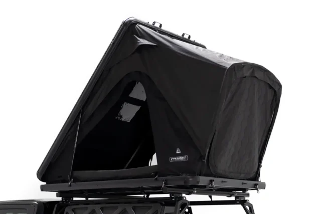 A black rooftop tent is mounted on a vehicle's roof rack, partially open with a zippered entrance and a small window visible on the side—perfect for your next adventure, as featured in Overland News.