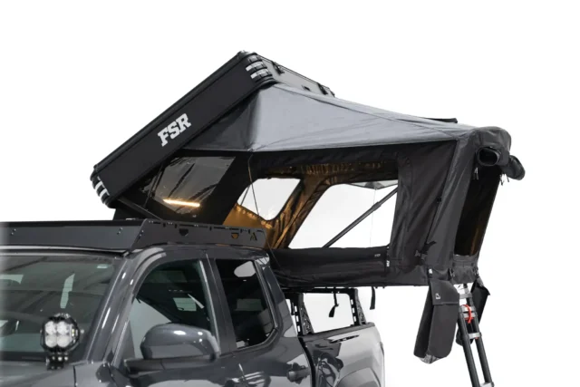A black rooftop tent labeled FSR is mounted on top of a gray pickup truck, partially open with windows and support poles visible, set against a plain white background—perfect for your next Overland News adventure.
