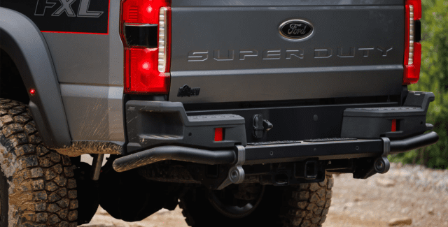 Close-up of the rear end of a gray Ford Super Duty FX4 pickup truck with muddy off-road tires, featured in Overland News, showing the tailgate, bumper, and rear lights on a dirt trail.