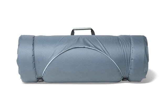 A rolled-up gray sleeping bag with a handle on top, secured by two black straps, rests on a white surface—perfect for your next Overland News adventure.