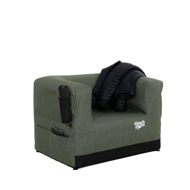 A green inflatable armchair with a black jacket draped over its backrest, a cup holder containing a bottle on one arm, and a side pocket—featured in Overland News—boasts the “slouch couch” logo on the front.