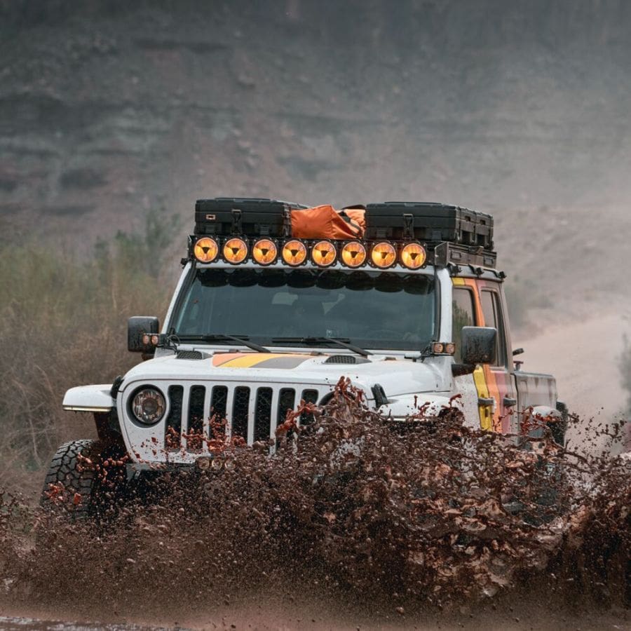 off-road vehicle driving through mud with row of accessory lighting