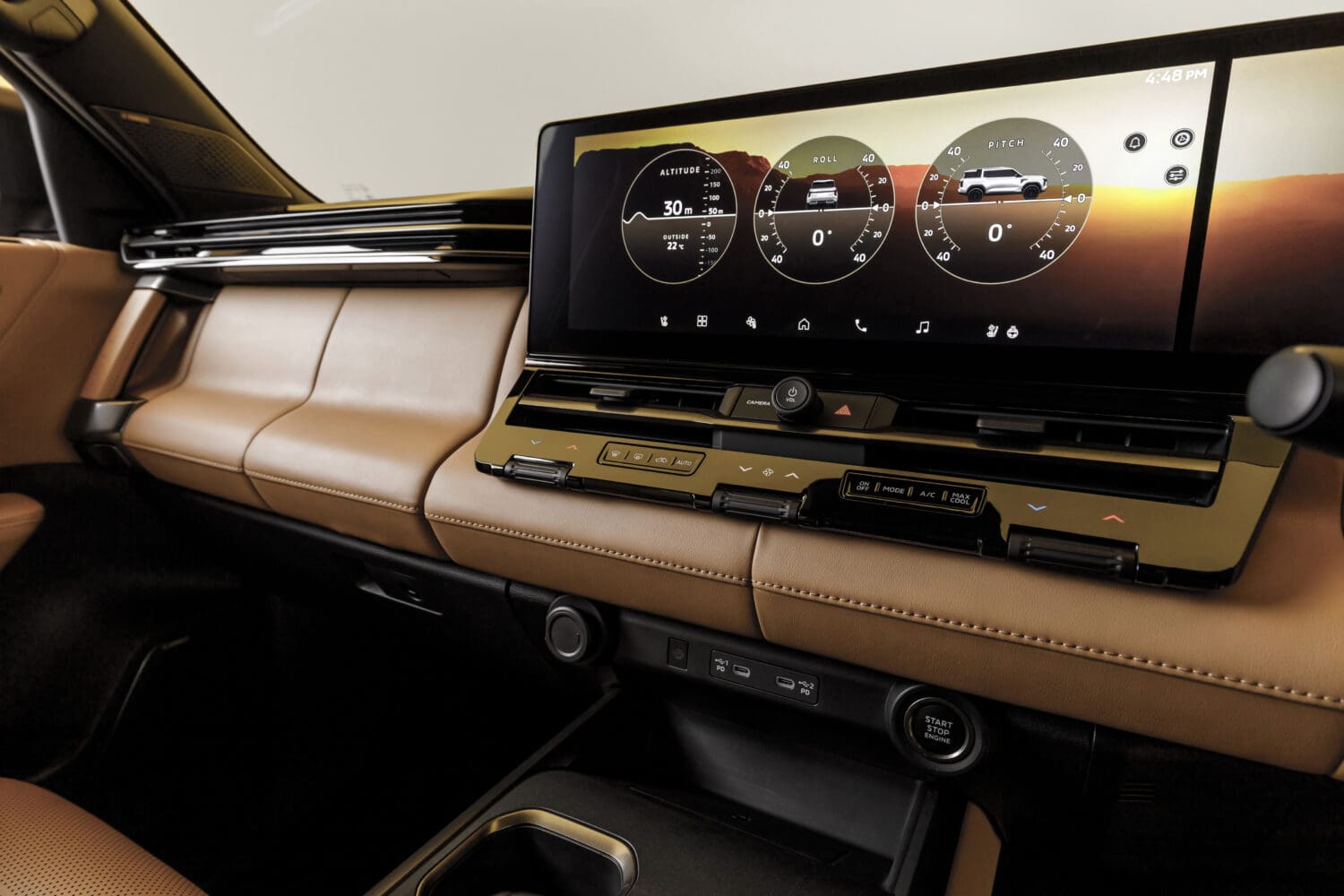 Close-up of a Mitsubishi Pajero’s front interior showing the dashboard, brown leather seats, a wide touchscreen displaying vehicle data, air vents, and push-button start.
