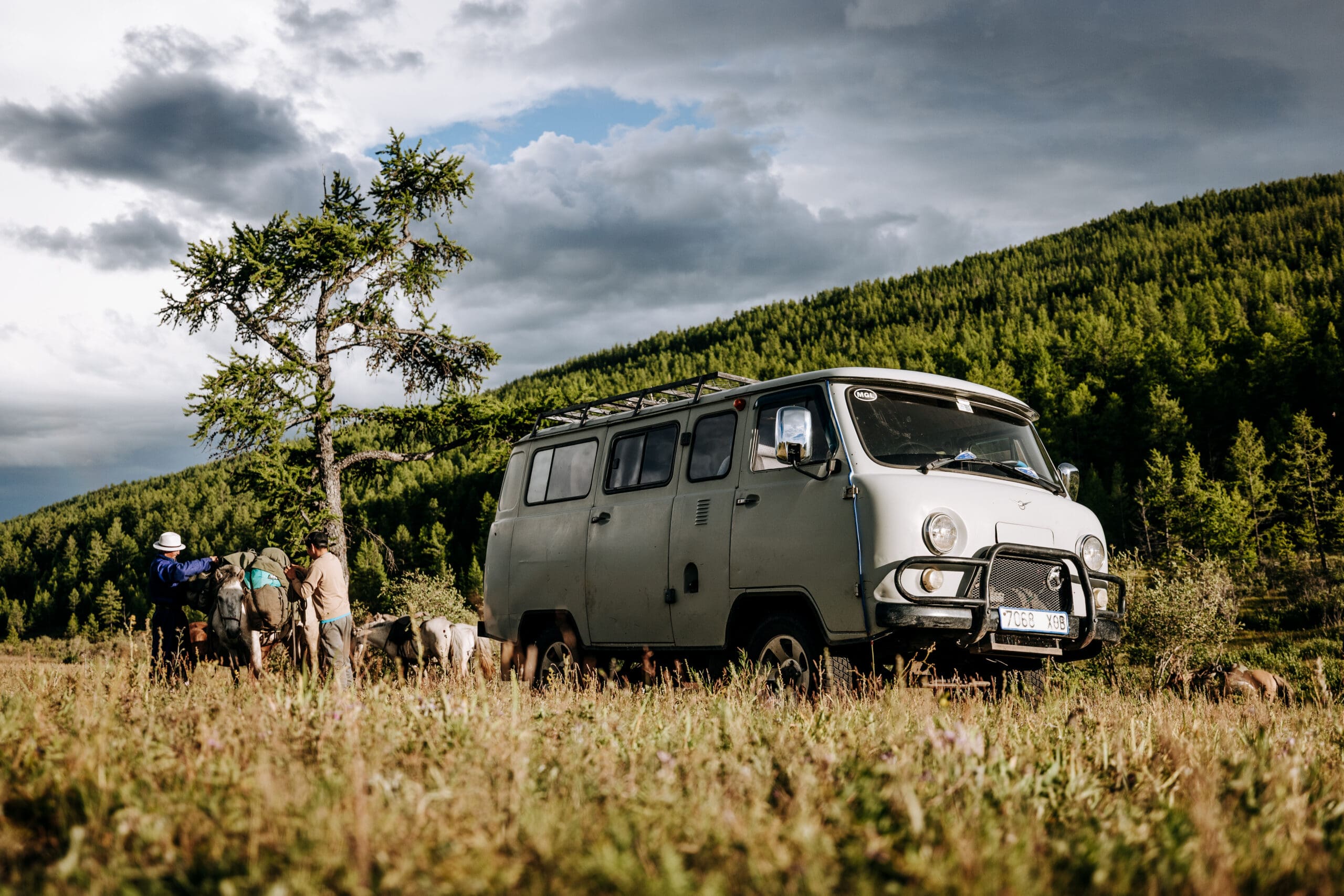 uaz vehicle parked in a field with horses and two mongolian men