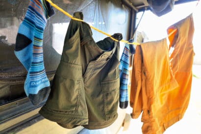 Blue socks, green shorts, and an orange shirt hang on a yellow clothesline outside, drying in the sunlight with a blurred background—just another day of laundry at camp.