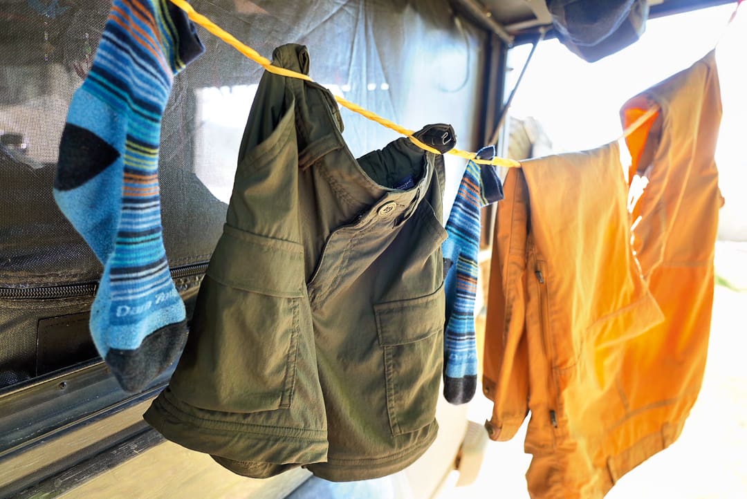 Blue socks, green shorts, and an orange shirt hang on a yellow clothesline outside, drying in the sunlight with a blurred background—just another day of laundry at camp.