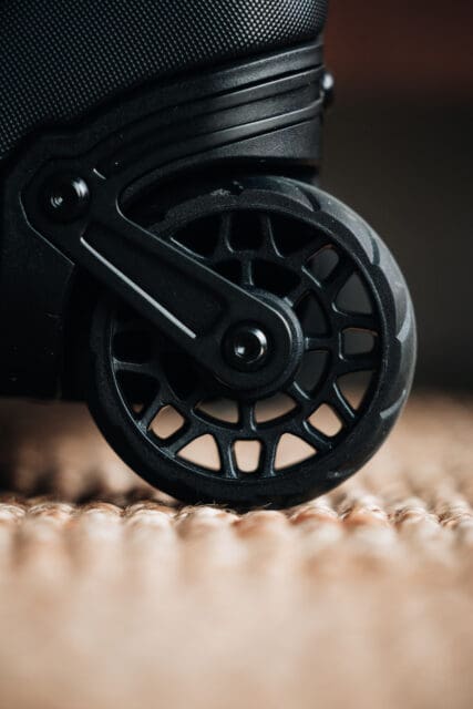 Close-up of a black luggage wheel with a modern, spoke-like design, resting on a textured, woven surface—highlighting the sleek engineering often found in premium options like the Pelican ATX Aegis Carry-On.