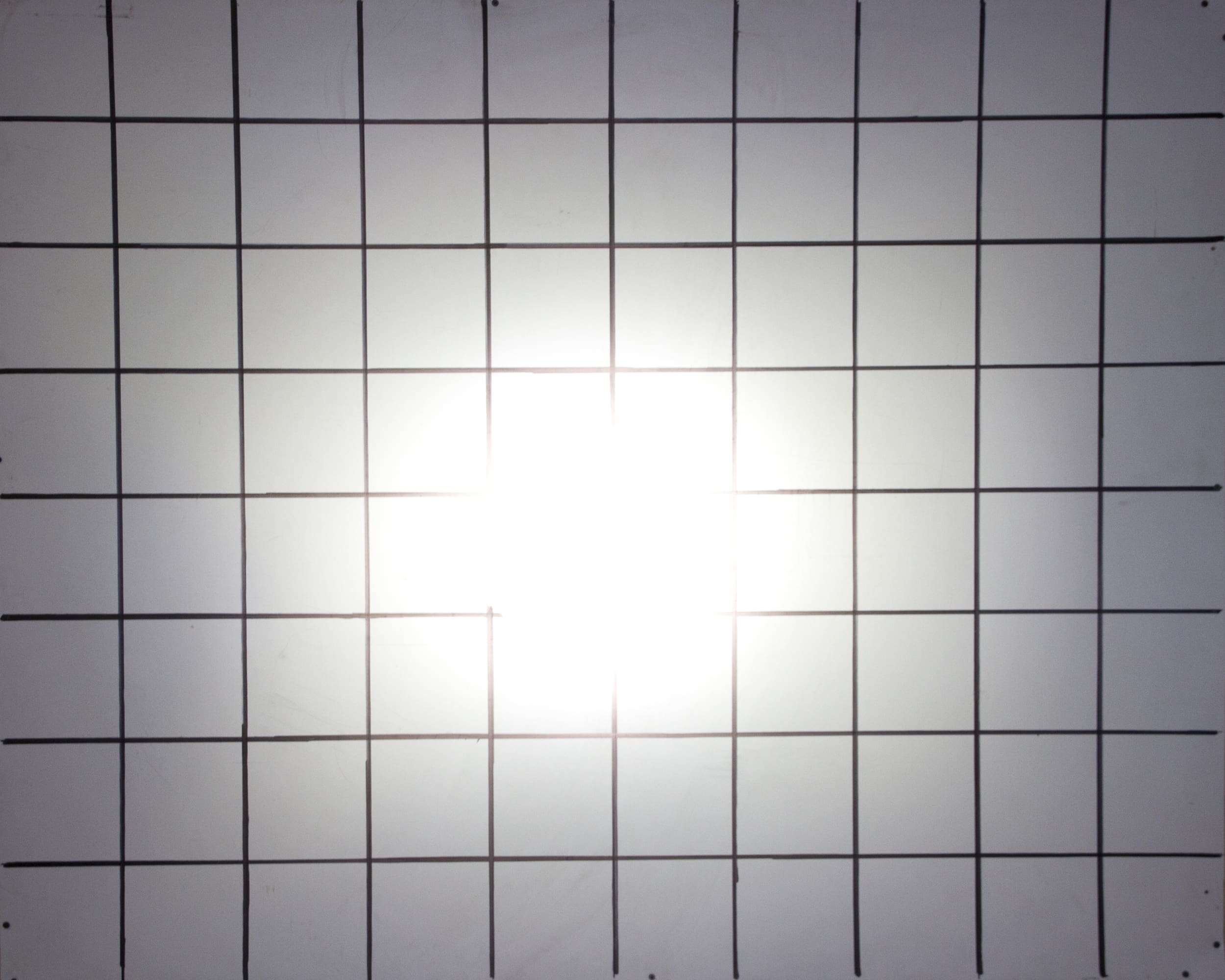 A bright white light, reminiscent of high-intensity driving lights, shines at the center of a grid pattern made of evenly spaced black lines on a white surface.