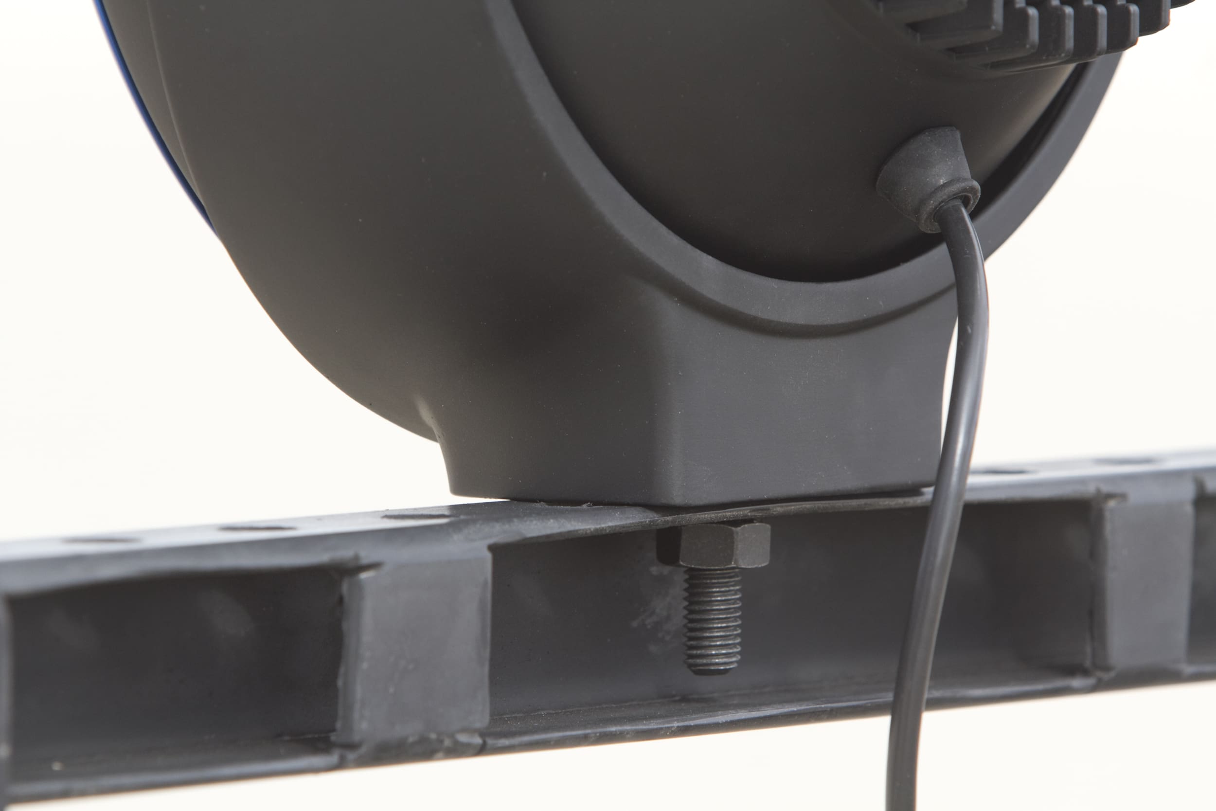 Close-up of a black electronic device mounted on a metal rail with a visible screw and a connected cable, often found in setups for driving lights. The focus is on the mounting hardware and part of the device’s housing.