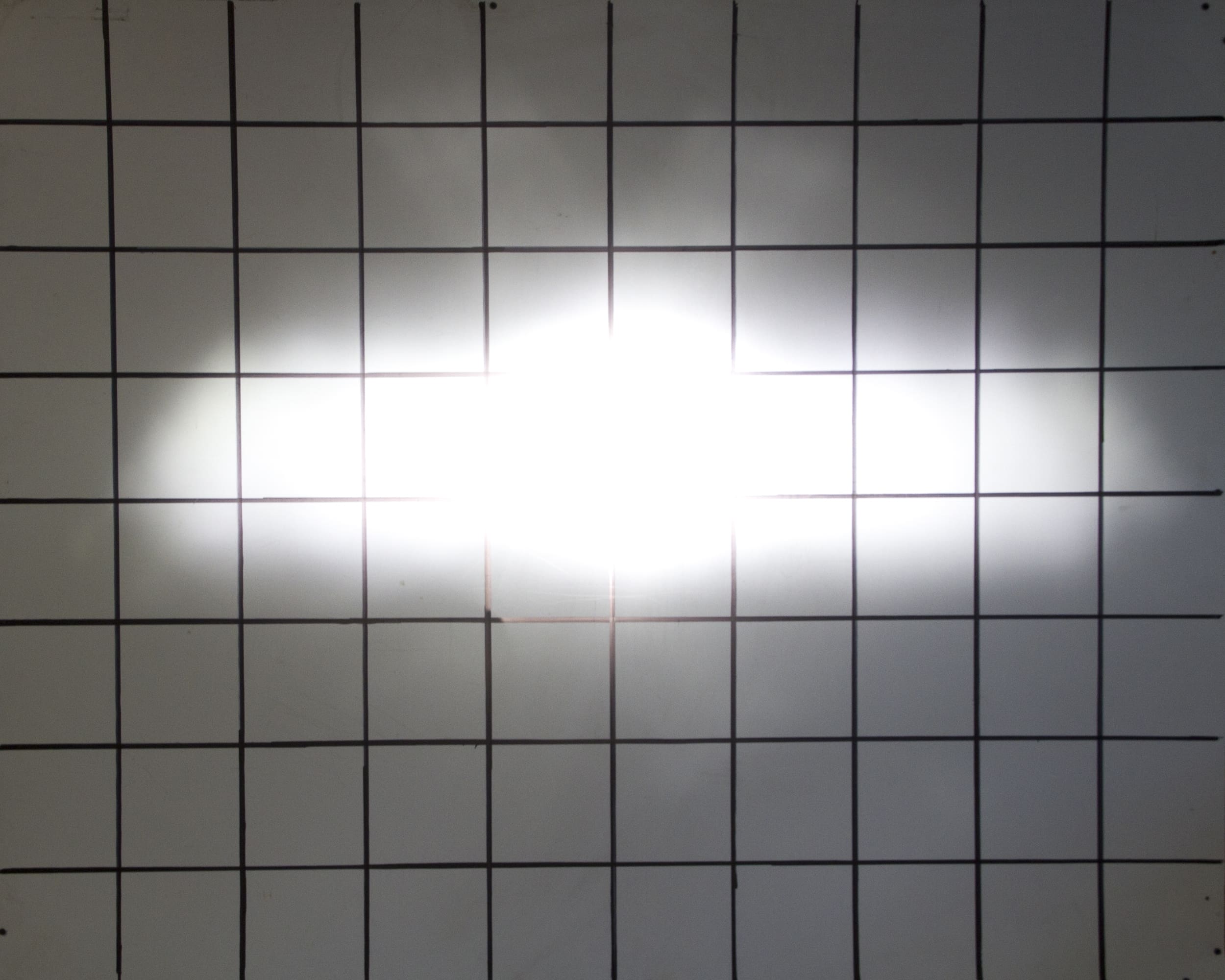 A bright white driving light shines at the center of a black grid on a white background, creating a horizontal glow that obscures the grid lines near the middle.