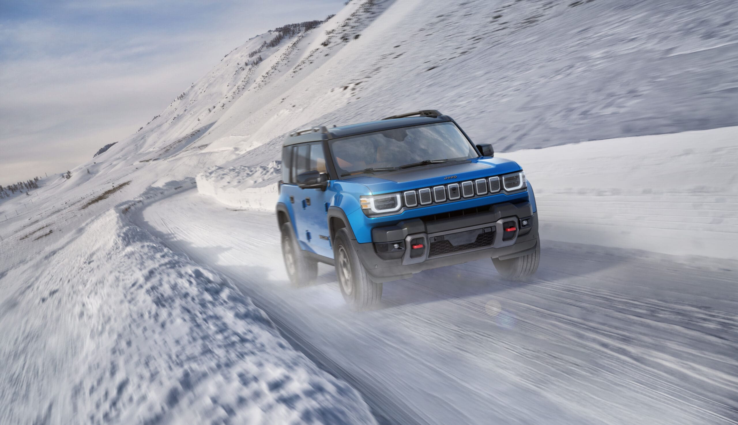 A bright blue Jeep Recon SUV drives on a snowy mountain road, surrounded by tall snowbanks and white, sloping hills under a cloudy sky.