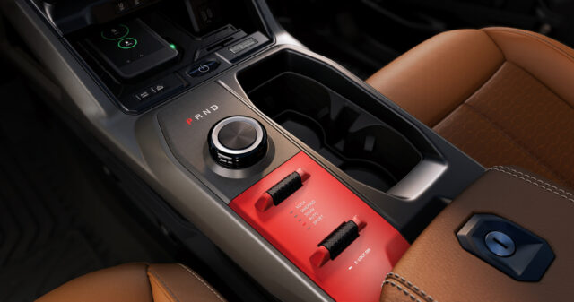 Close-up of a Jeep Recon’s center console featuring a rotary gear selector, drive mode switches, cup holders, and part of a brown leather seat.