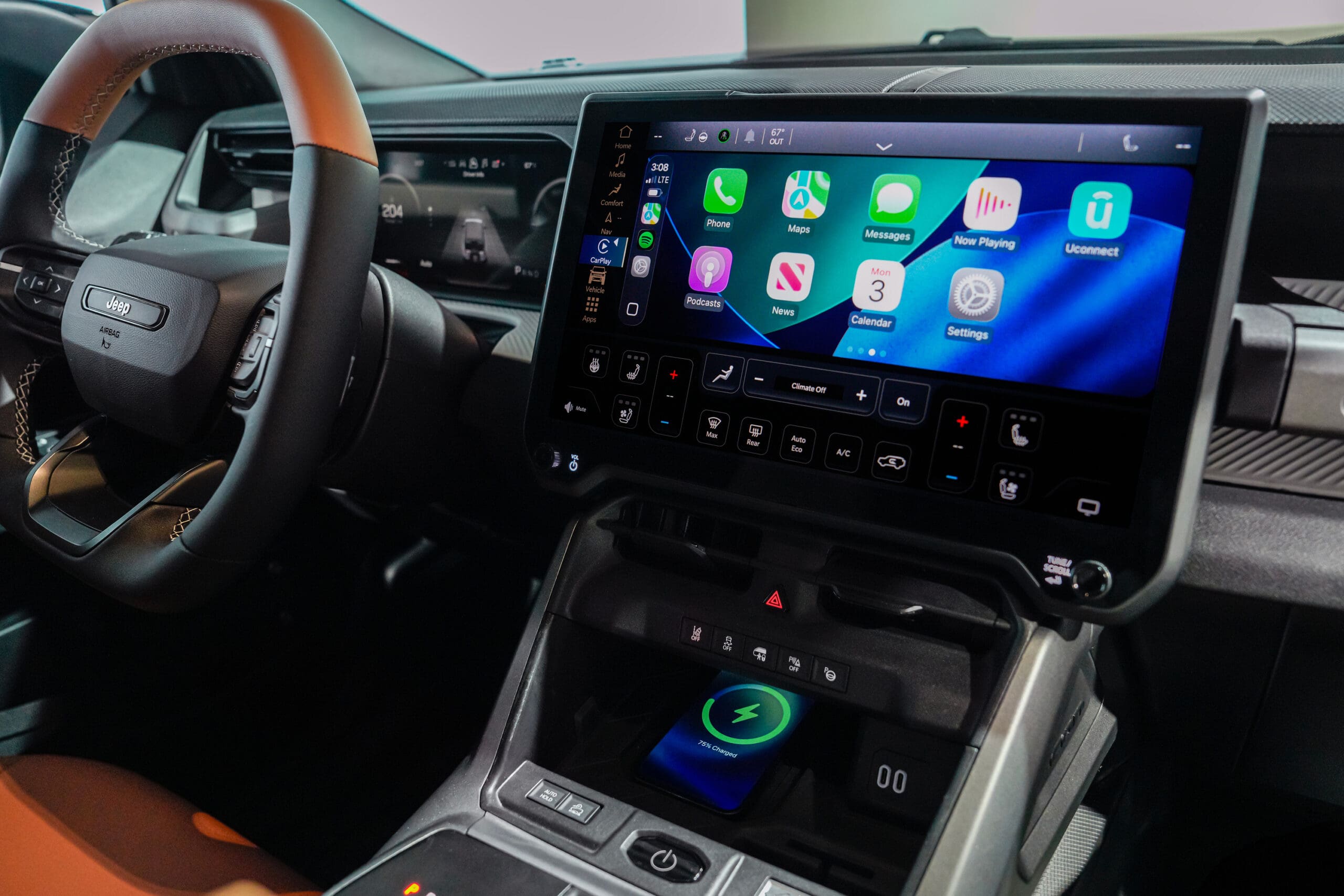 Close-up of a modern Jeep Recon interior showing a large touchscreen display with Apple CarPlay, wireless charging pad, and part of the steering wheel.
