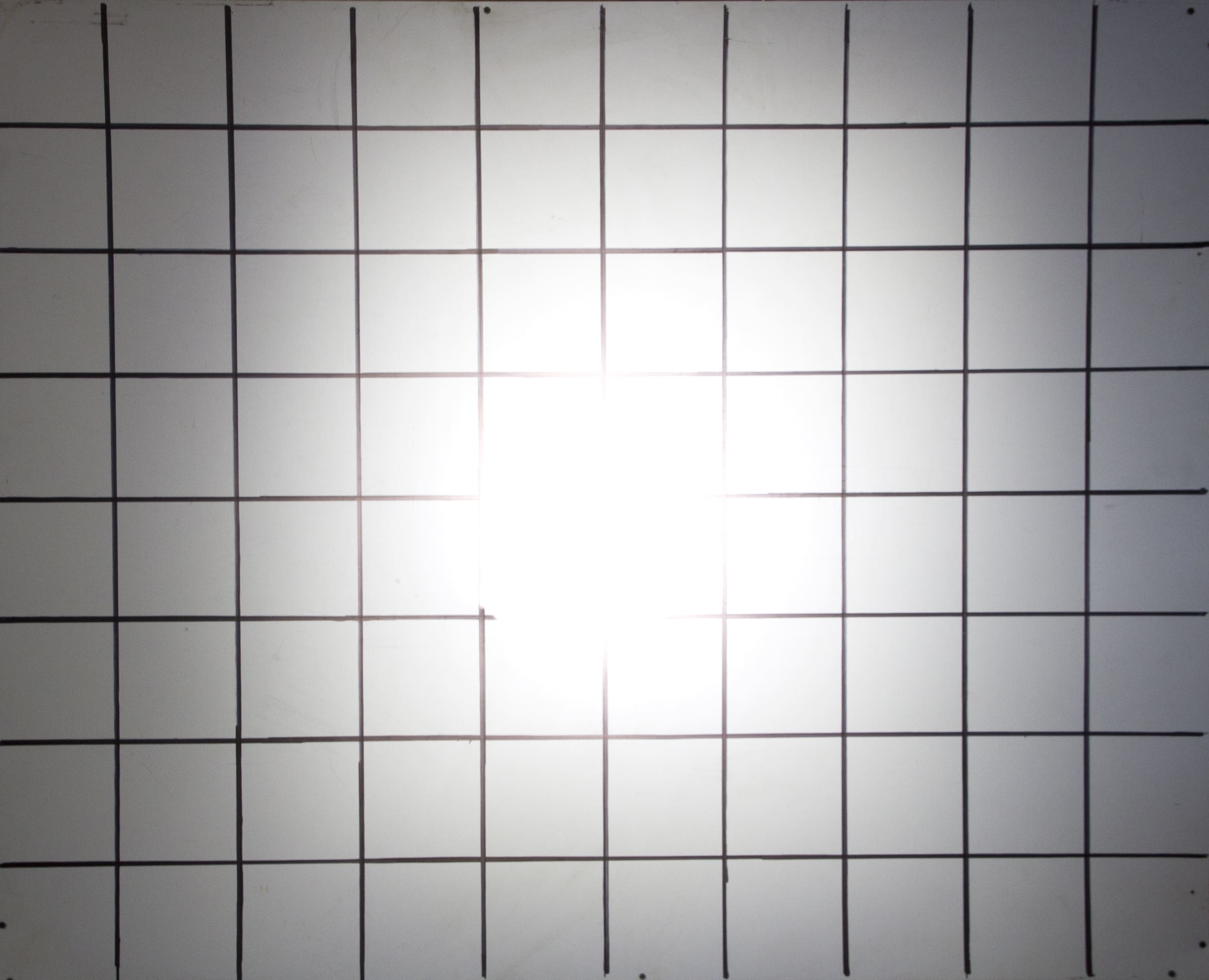 A whiteboard with a black grid pattern and a bright light, similar to driving lights, shining at the center, causing some glare and making the middle squares hard to see.