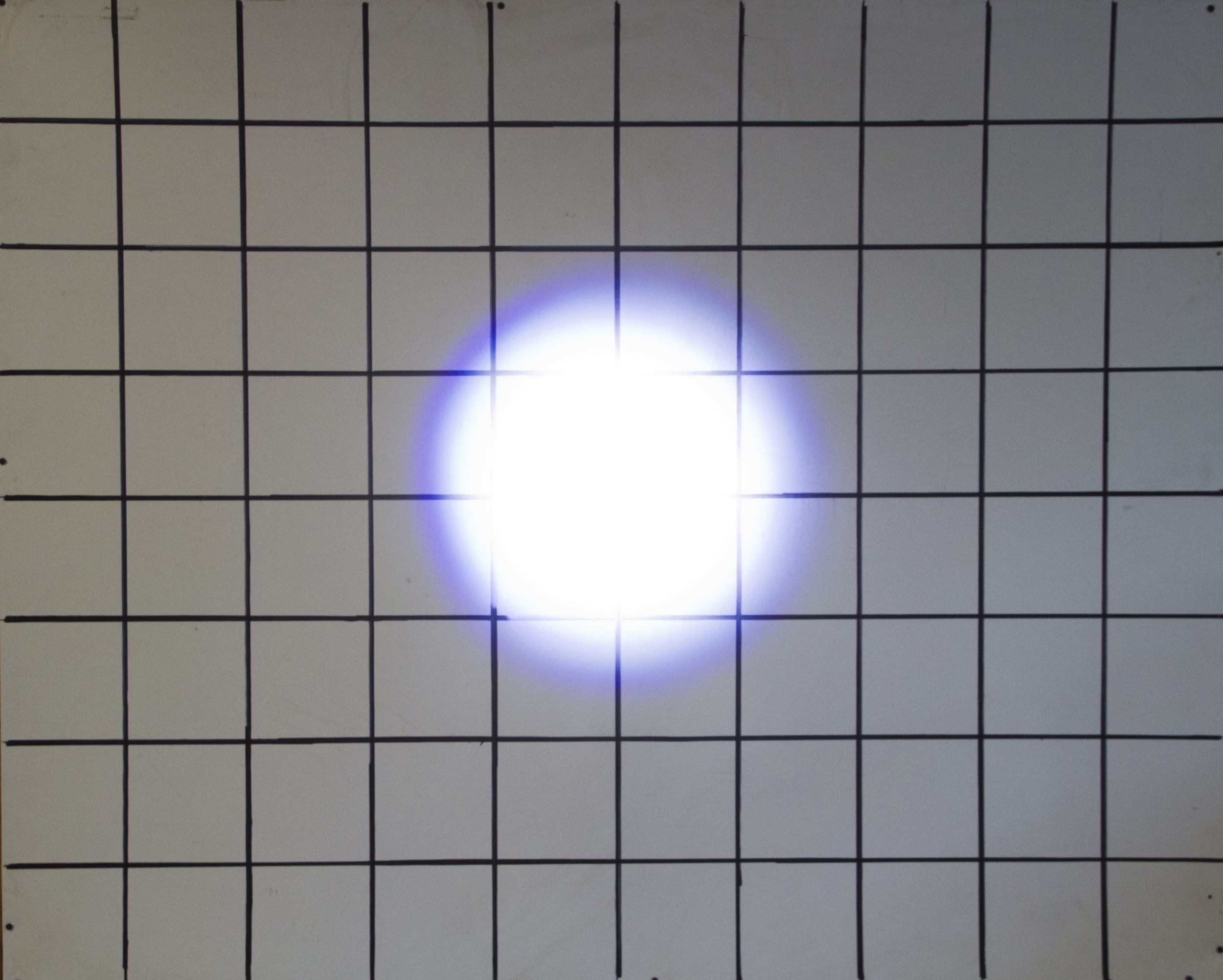 A white grid on a wall with a bright white light, similar to powerful driving lights, shining at the center and creating a blue halo effect around the light source.