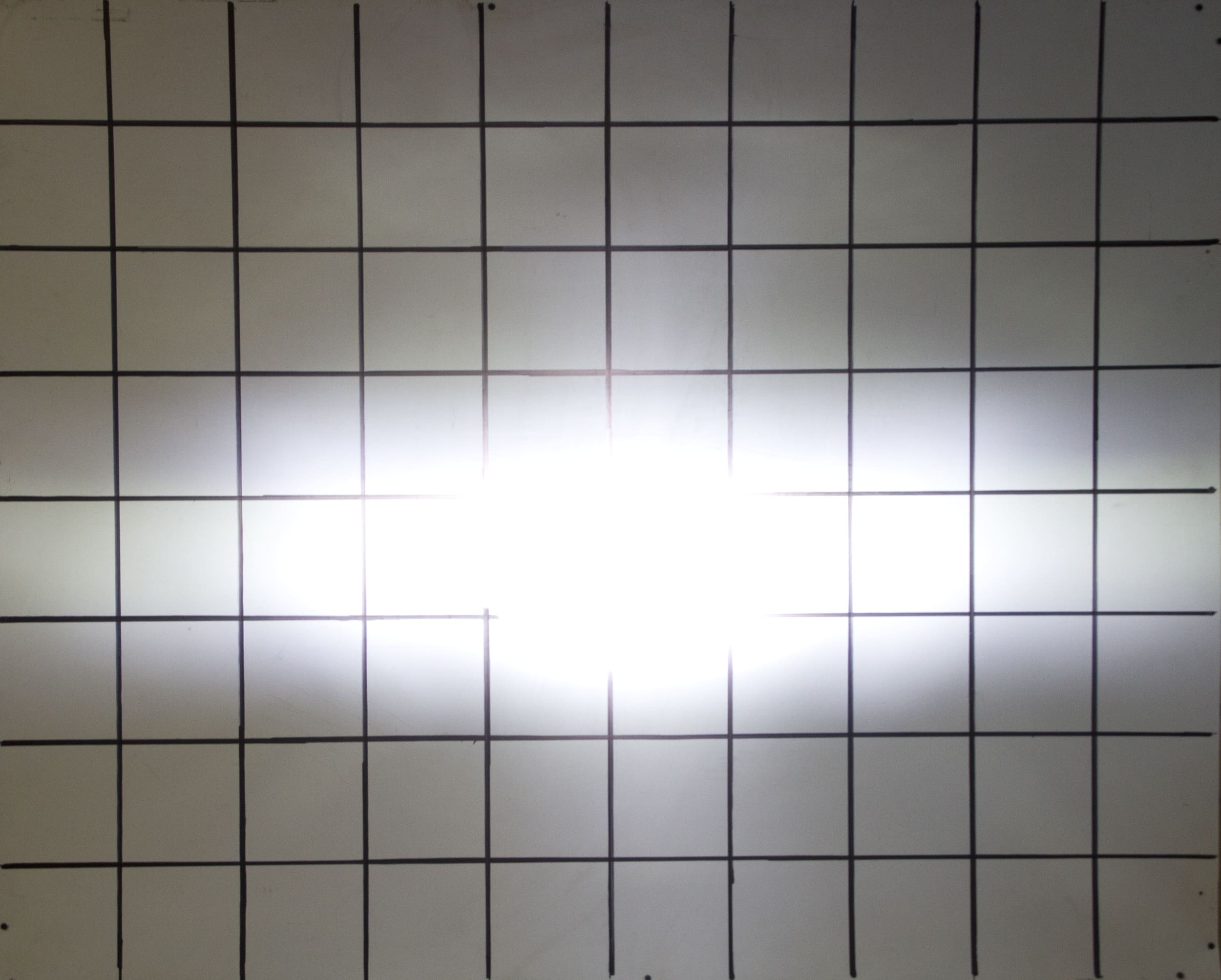 A bright white driving light shines at the center of a grid made of black lines, creating a glare that obscures the grid in the middle of the image.