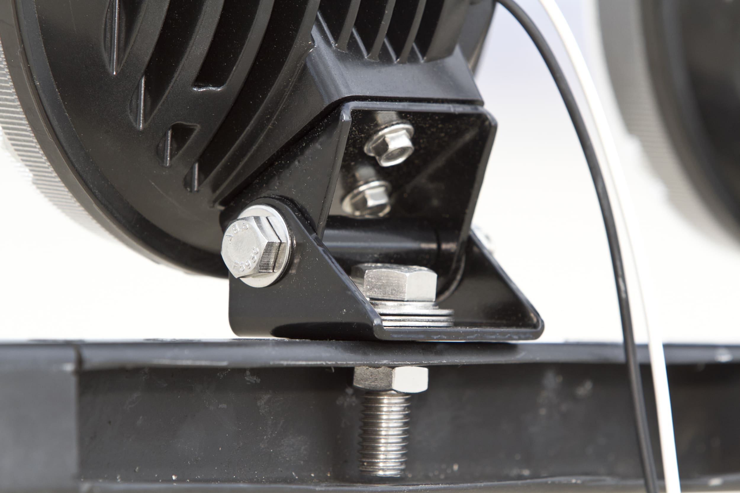 Close-up of a metal bracket with bolts and a black wire, mounted onto a black surface, possibly part of driving lights or another mechanical device.