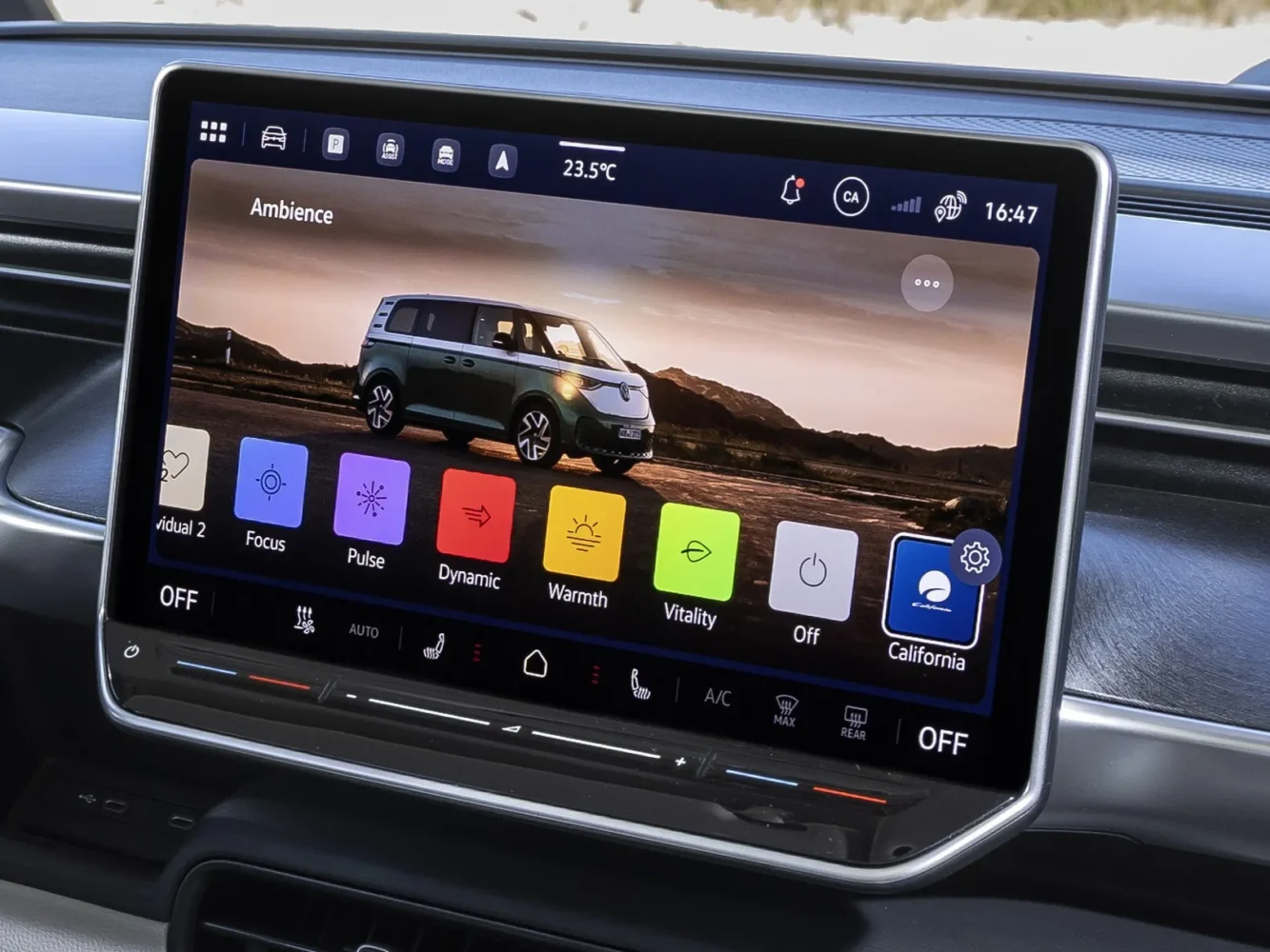 A car infotainment screen displays climate settings and ambient lighting options, with a photo of a fully electric VW California campervan on a scenic background visible on the main display.
