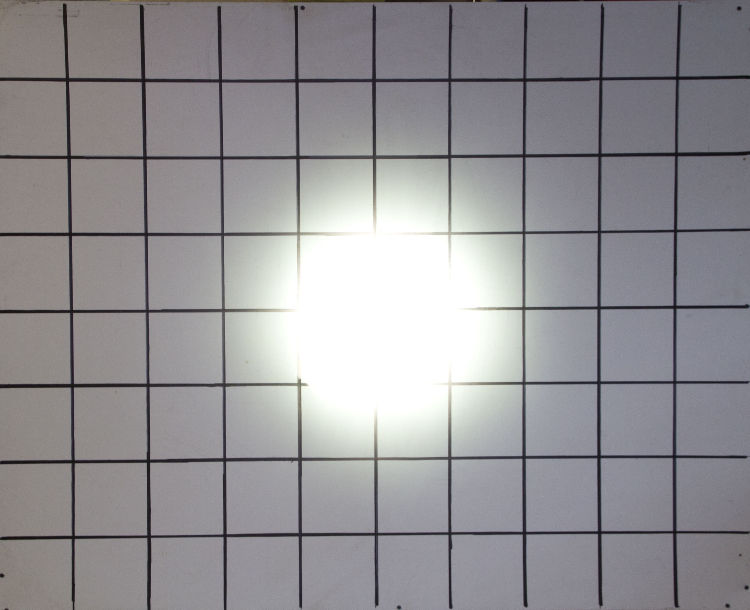 A white grid with black lines is shown on a flat surface, with a bright white light source—resembling powerful driving lights—shining at the center, causing a strong glare and obscuring some grid squares.