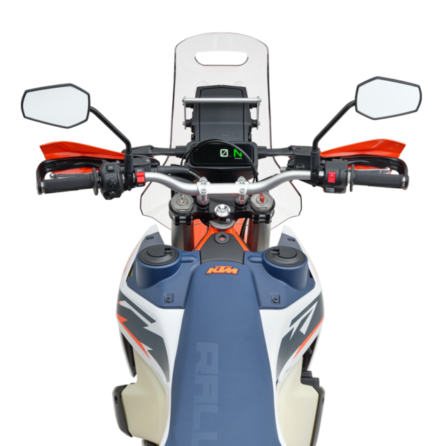 View from above of a 2027 KTM 690 Rally motorcycle’s handlebars, dashboard, and seat, showing mirrors, handguards, and digital display, with a blue seat and orange accents.