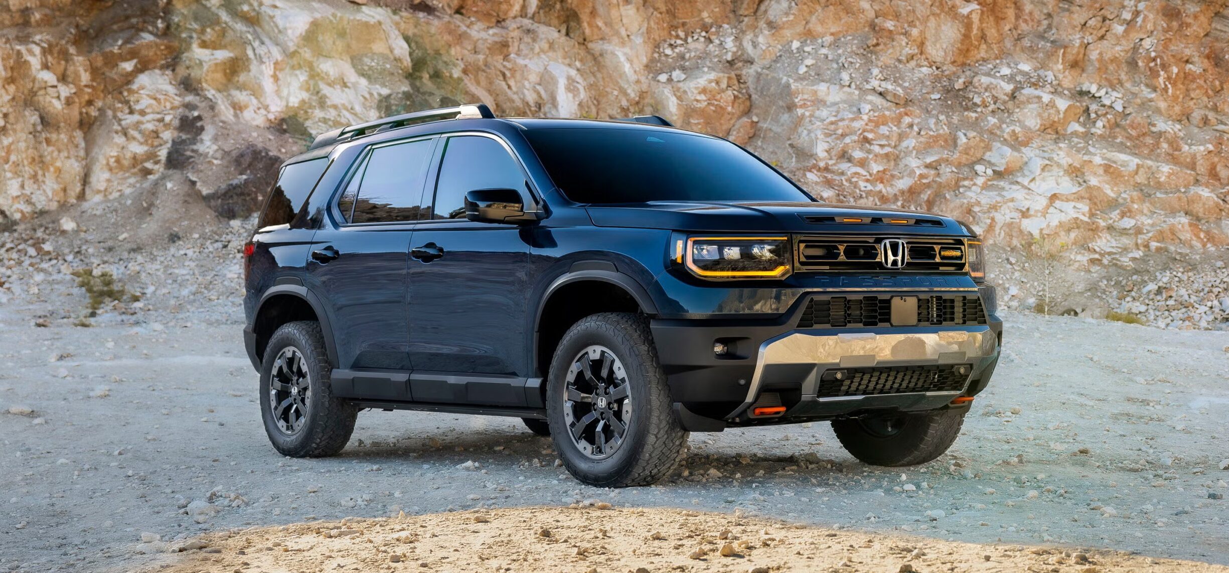 A black SUV is parked on rocky terrain with a stone cliff in the background. The vehicle appears clean and modern, reflecting sunlight on its windows and surface—an ideal scene for any Overland News feature.