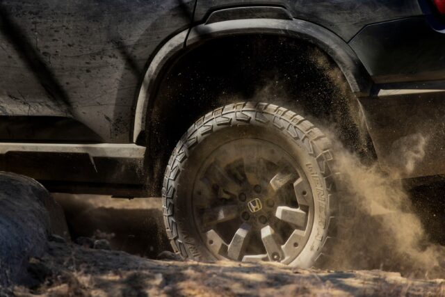 A close-up of a Honda vehicle’s dirty rear tire kicking up dust as it drives over rough, rocky terrain—a perfect shot for Overland News enthusiasts.