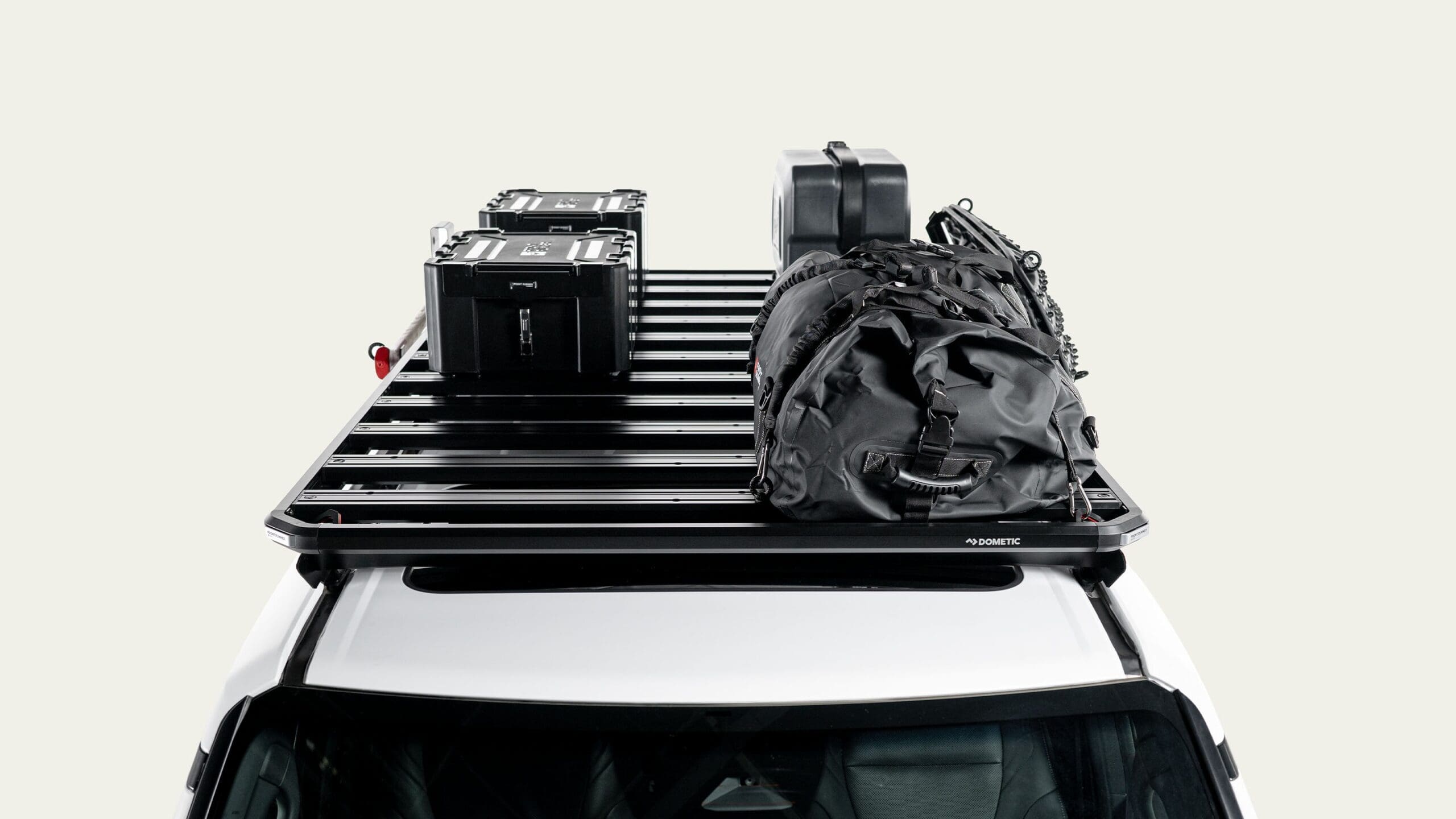 Top-down view of a white vehicle with a roof rack carrying two black hard cases, a black suitcase, and a black duffel bag, all secured and ready for transport—perfect for any Overland News adventure.