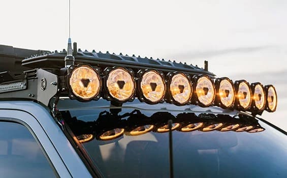A row of round, orange off-road lights mounted on the roof of a vehicle, reflecting on the windshield at sunset—perfectly capturing the spirit of adventure often featured in Overland News.