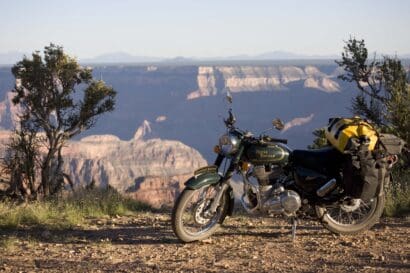A dark green Royal Enfield motorcycle with yellow gear bags parked on a dirt trail for adventure motorcycling overlooking the Grand Canyon.