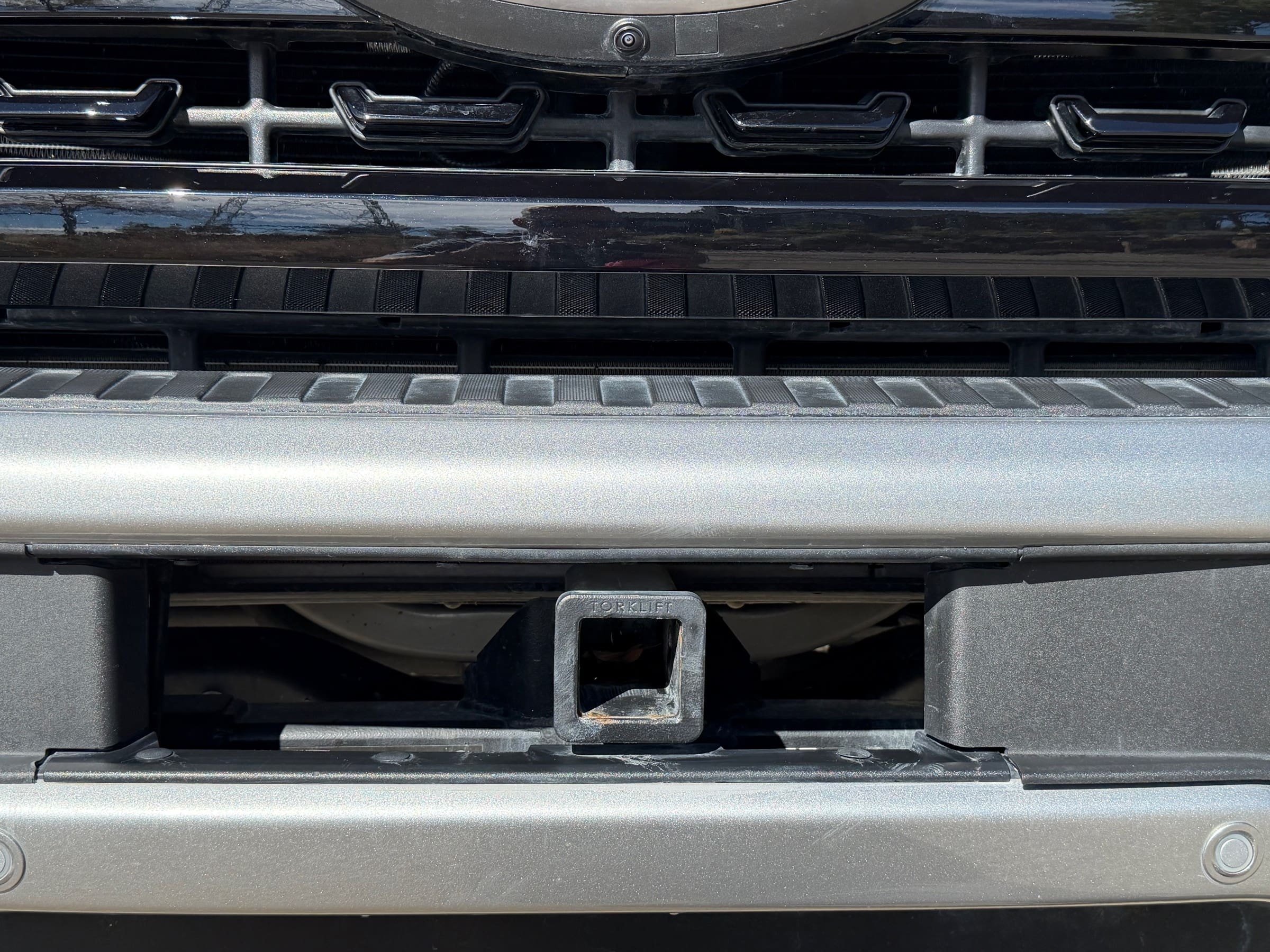Close-up of a trailer hitch receiver mounted in the center of a 2024 Ford F-350 front bumper.
