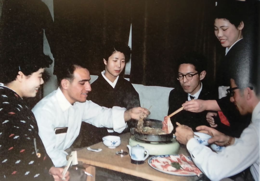 Five people gathered around a table, cooking and sharing food from a hot pot. The scene, reminiscent of the sociable spirit of the Omidvar brothers, is warm and lively with dishes and chopsticks in use.