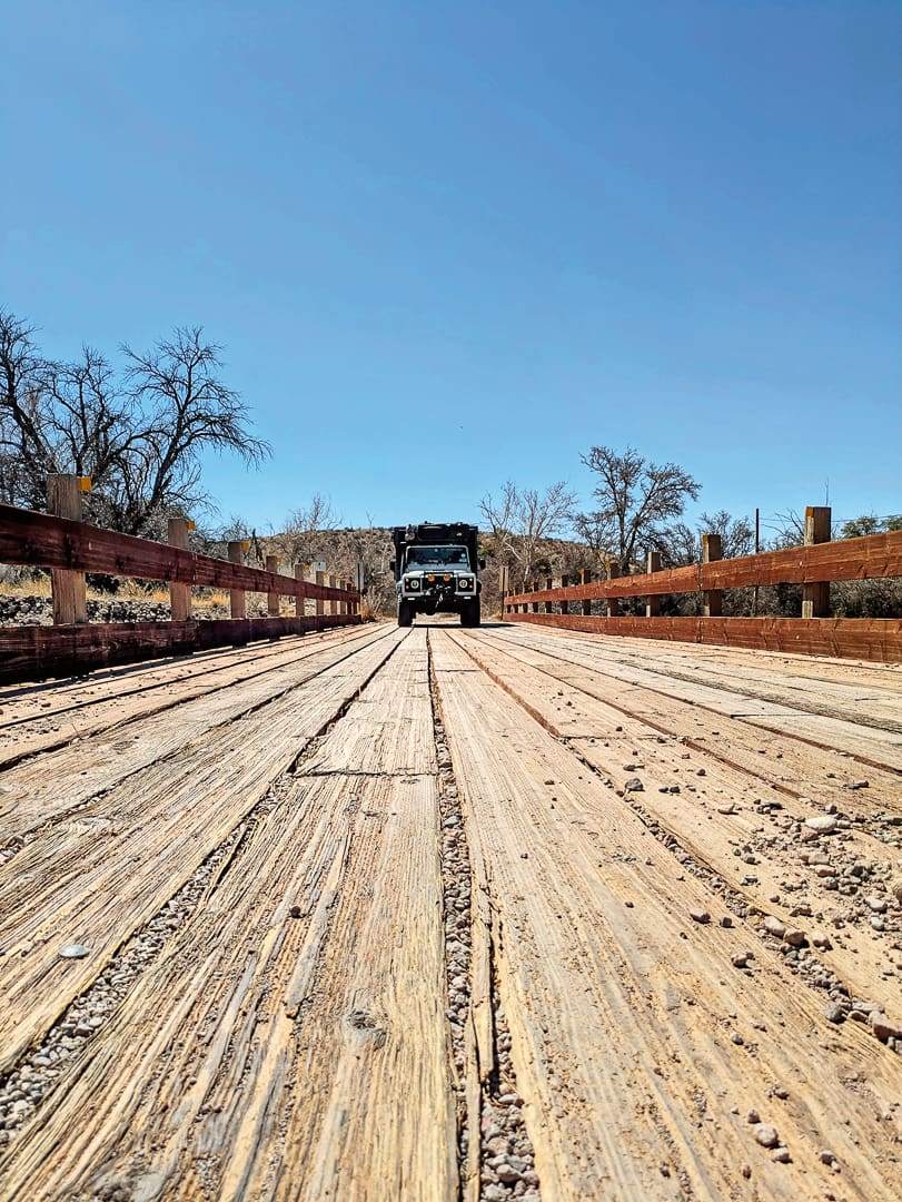 A white off-road vehicle with a roof rack drives across a wooden bridge on the Arizona Traverse.