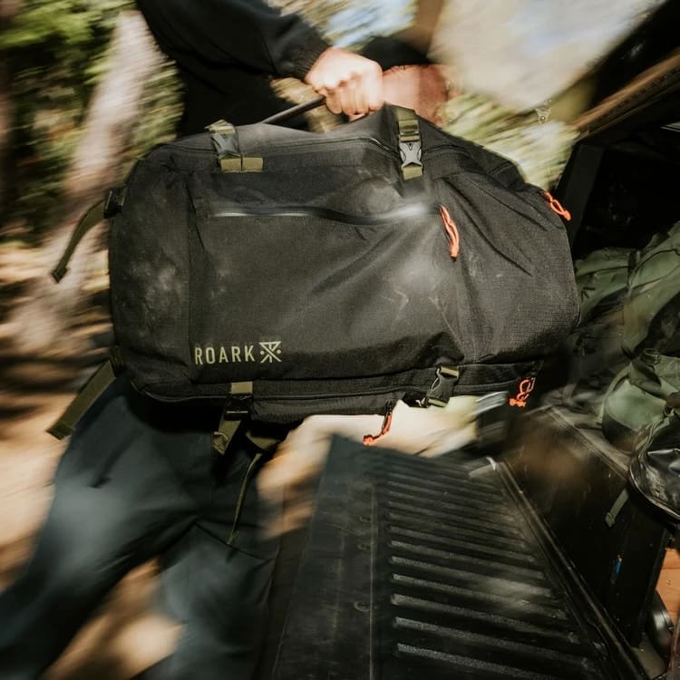 A person pulls a black Roark duffel bag out of the back of a truck for October 2026 overland news.