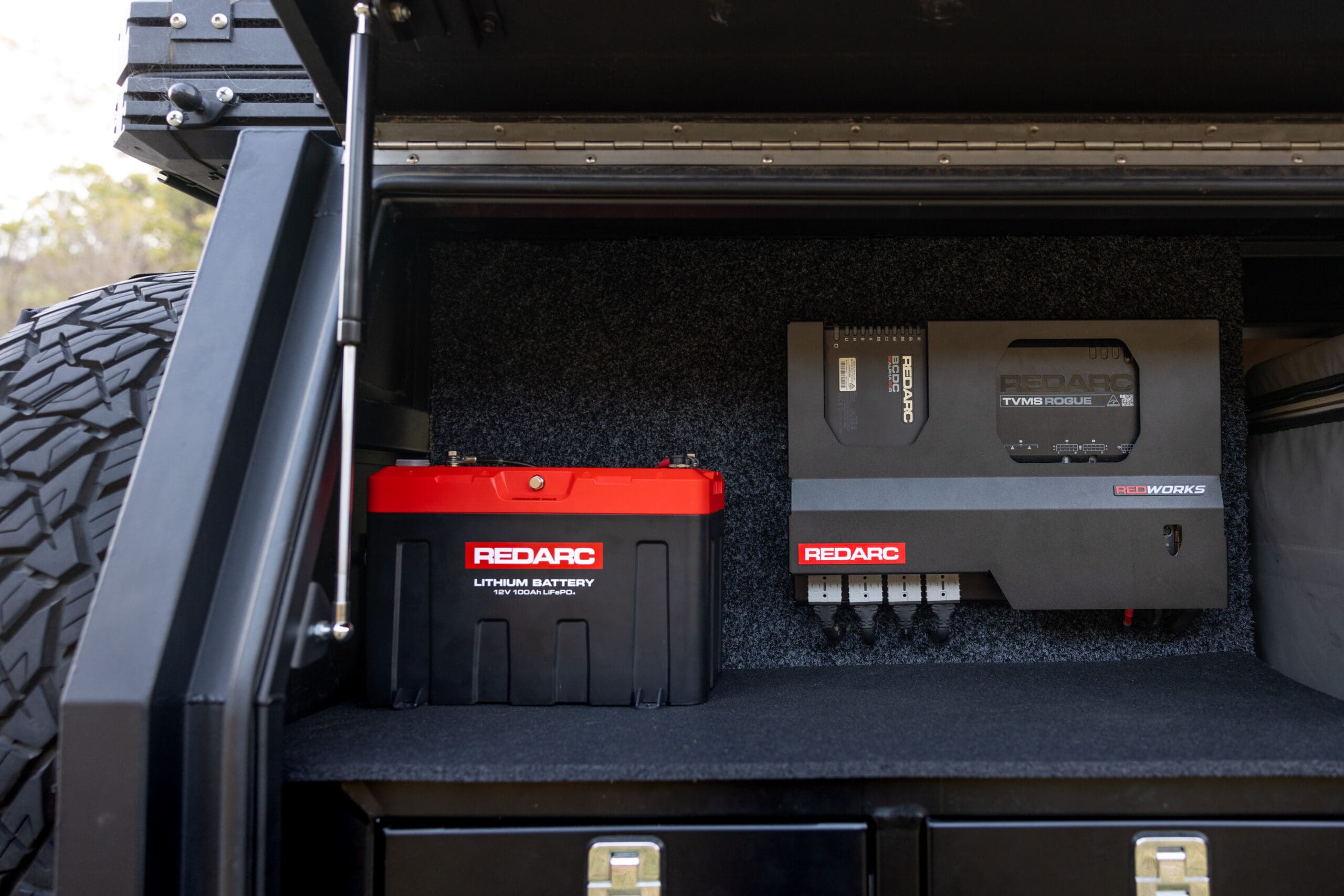 A REDARC lithium battery and TVMS Rogue power management system mounted inside a vehicle storage compartment, representing modern overland industry equipment.
