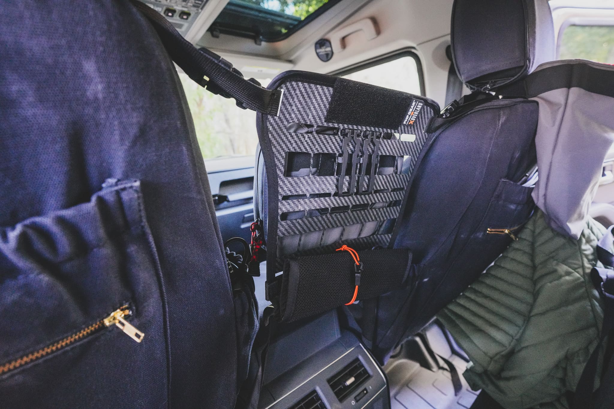Carbon fiber-patterned Drive Line Gear MOLLE storage panel strapped to the back of a vehicle seat.