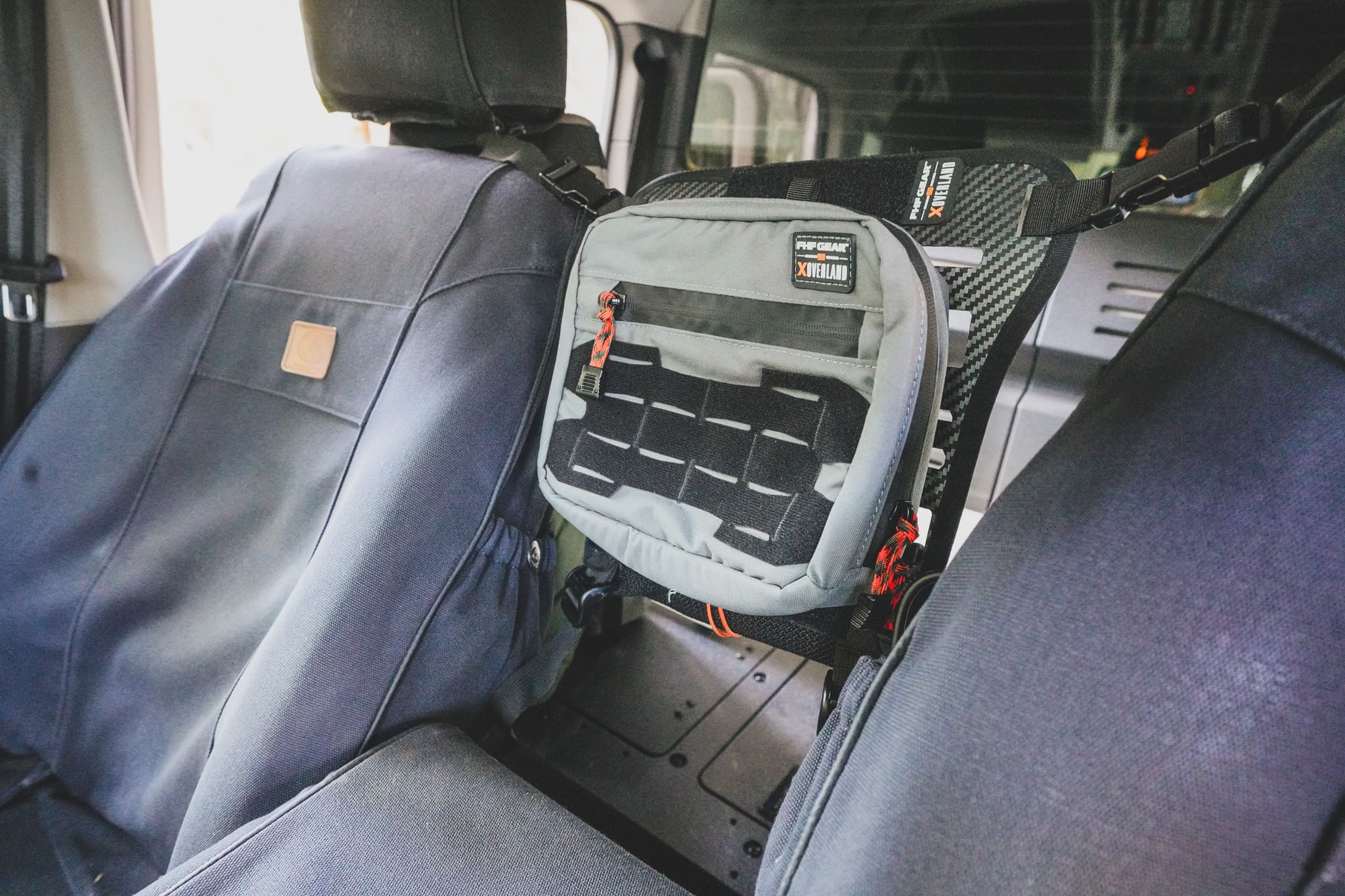 A gray XOVERLAND MOLLE-compatible storage pouch attached to the back of a vehicle seat.