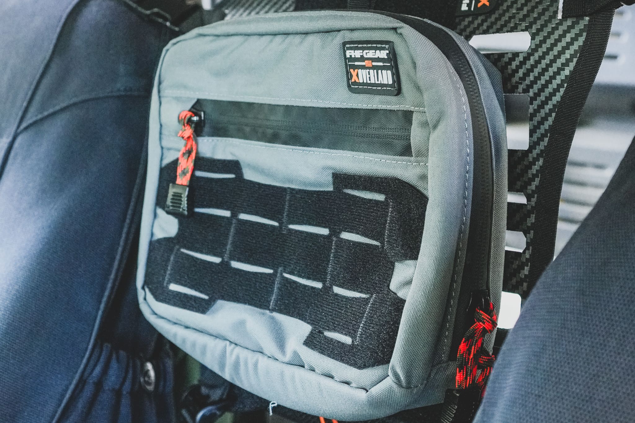 Gray tactical Drive Line Gear pouch with MOLLE webbing attached to a vehicle seat back, featuring an FHF Gear X Overland logo patch and red pull cords.