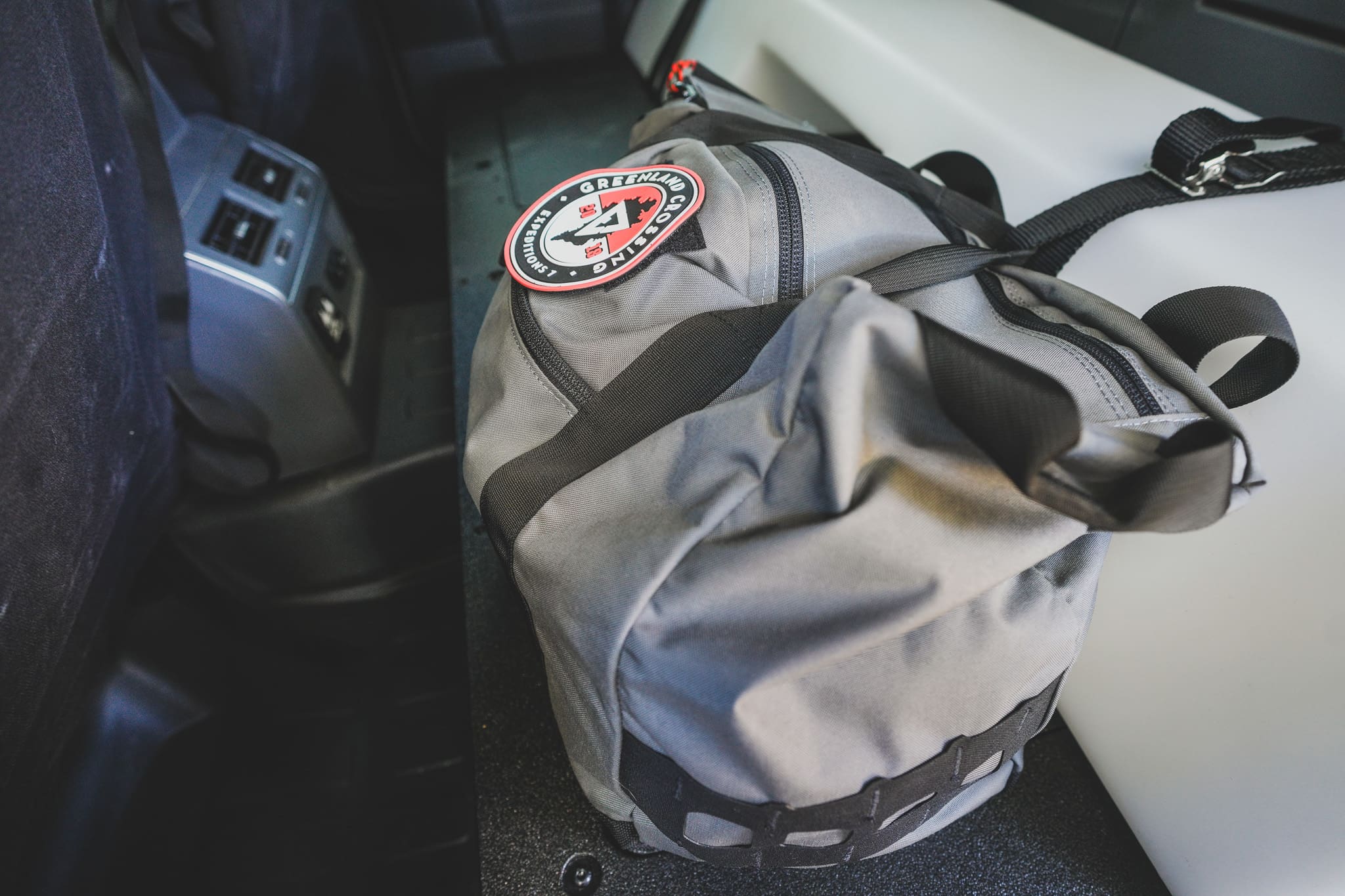 A grey XOVERLAND duffel bag with a circular Greenland Crossing Expeditions patch sits inside a vehicle.