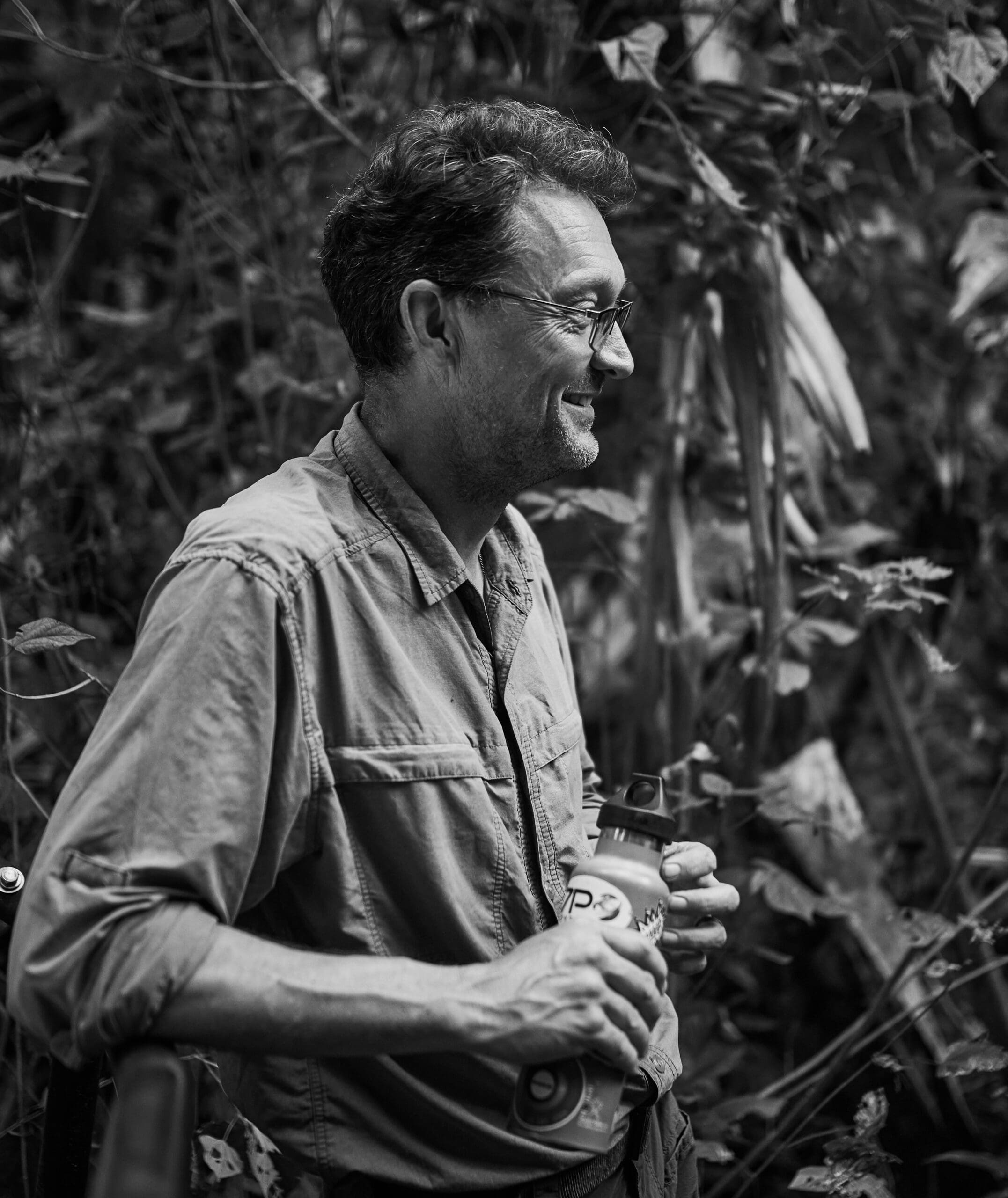 Graham Jackson smiles while holding a water bottle in a lush, wooded area during his adventure travel.