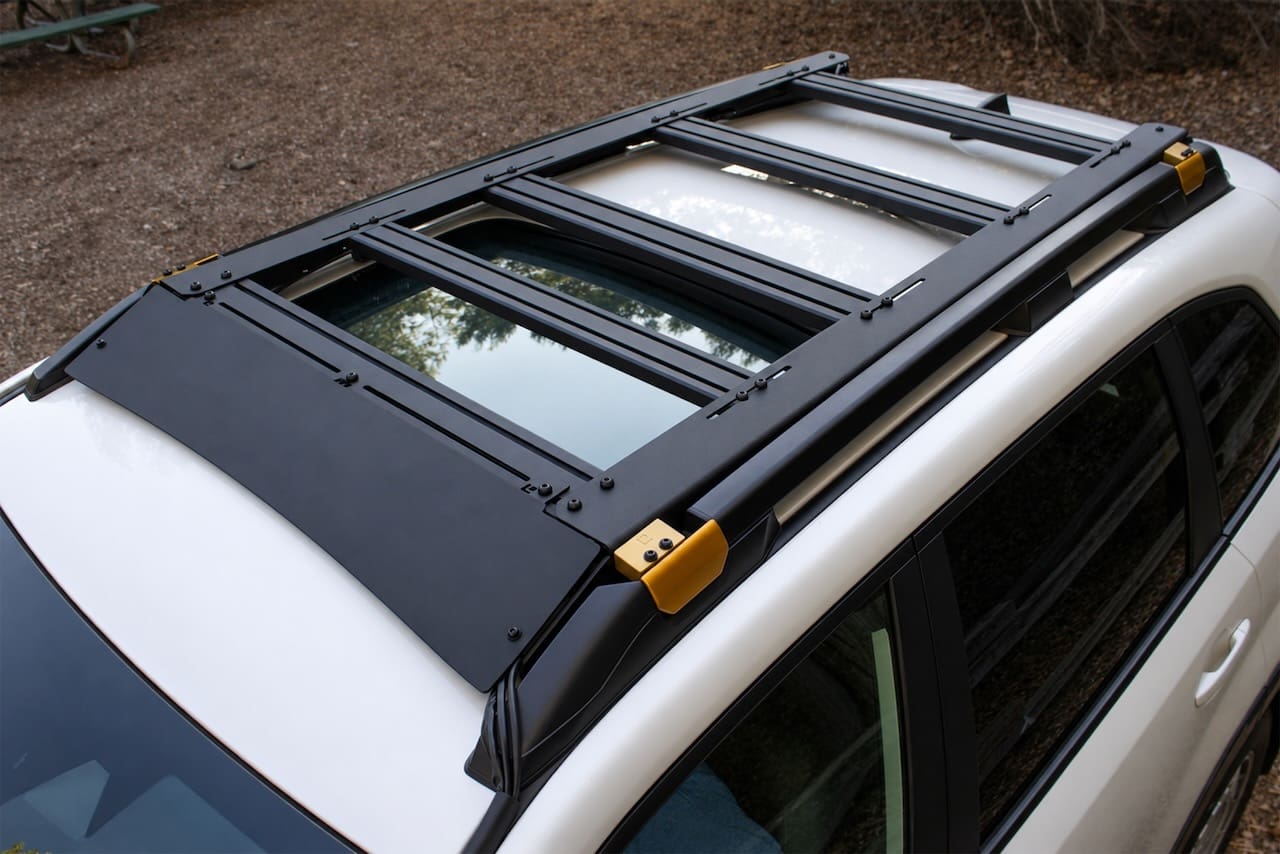 Black Leitner Designs metal roof rack with yellow accents mounted on the roof of a white vehicle.