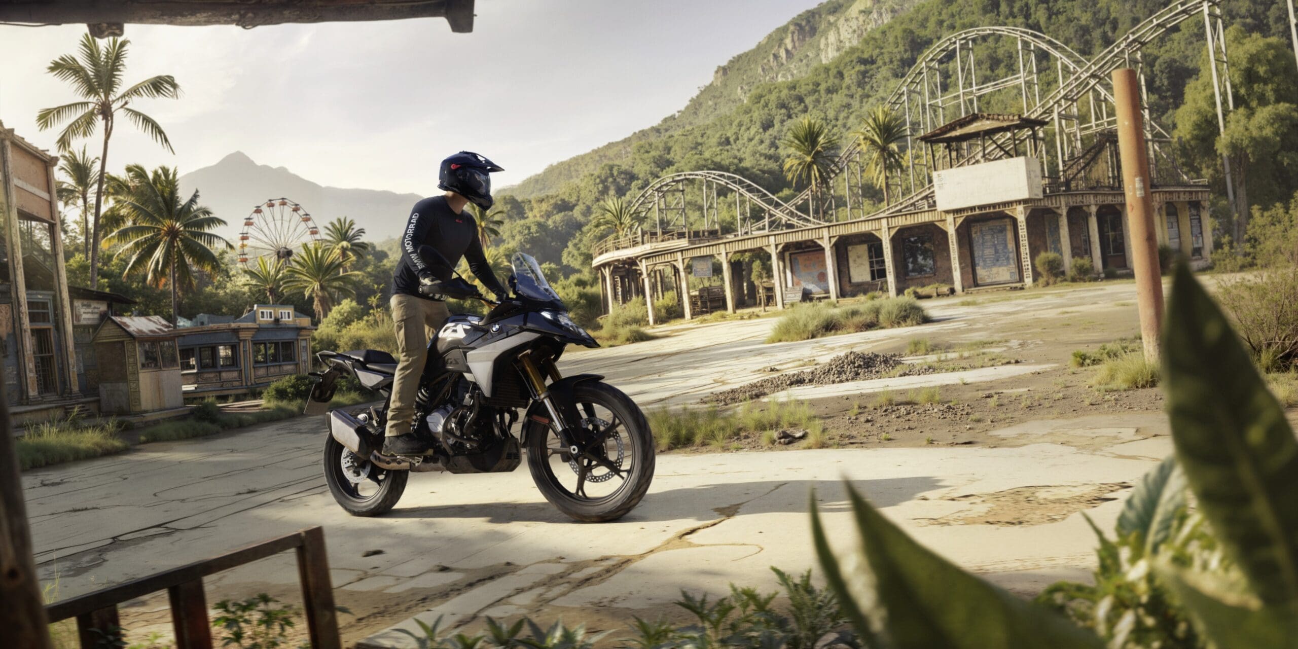 A motorcyclist wearing a helmet rides a black BMW Motorrad adventure motorcycle through an abandoned amusement park.