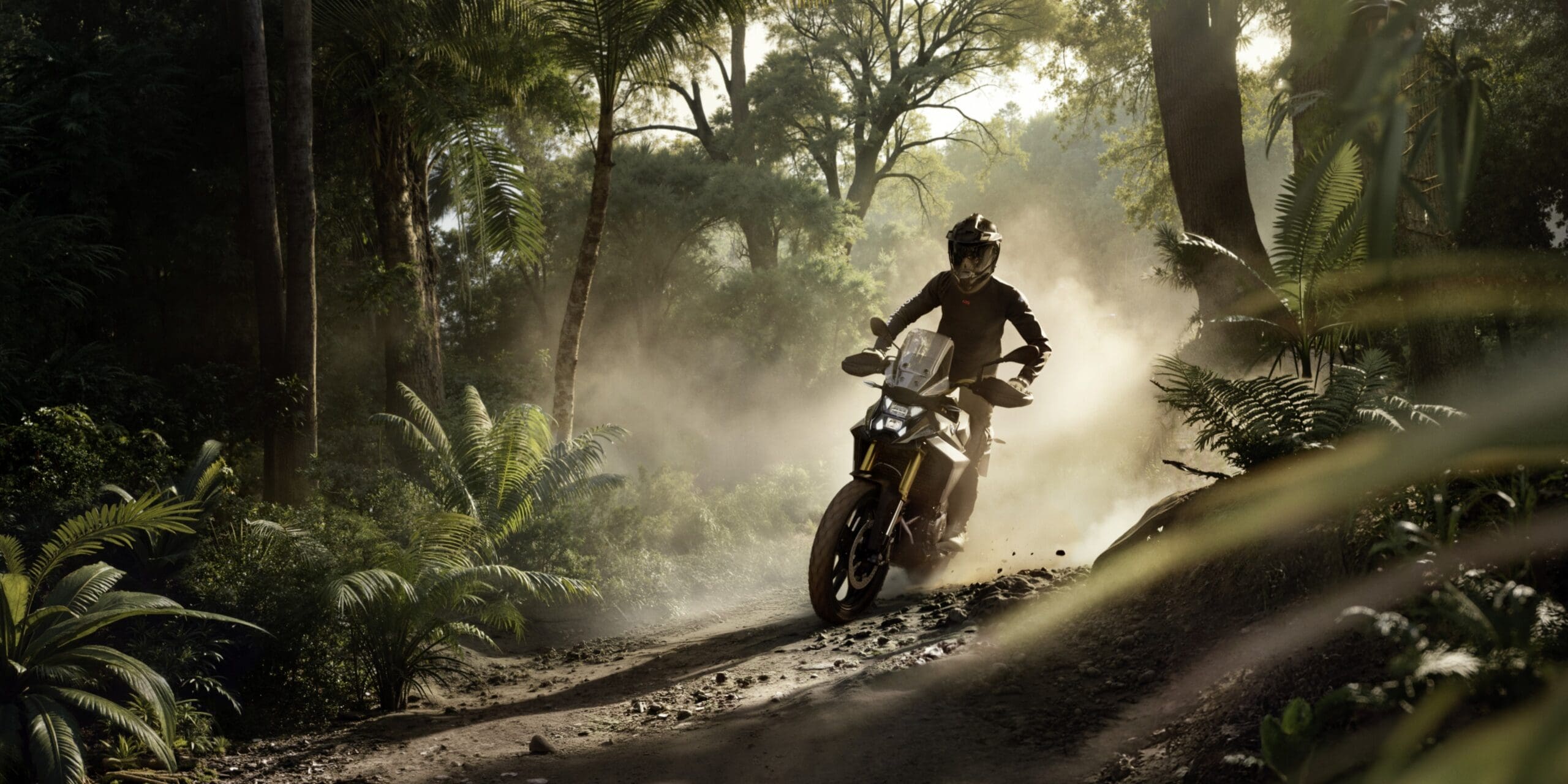 A person in safety gear rides a BMW Motorrad motorcycle along a dusty, sunlit dirt trail through a tropical forest.