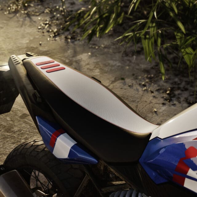 A close-up of a BMW Motorrad motorcycle seat featuring a white and black textured surface with three red rectangular accents.